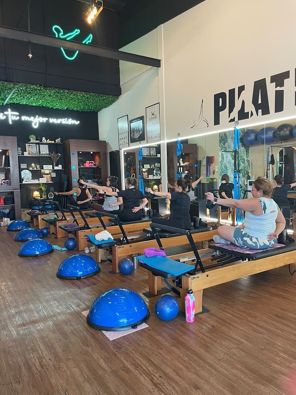 Alumnas sentadas en el Reformer haciendo una torsión con los brazos extendidos