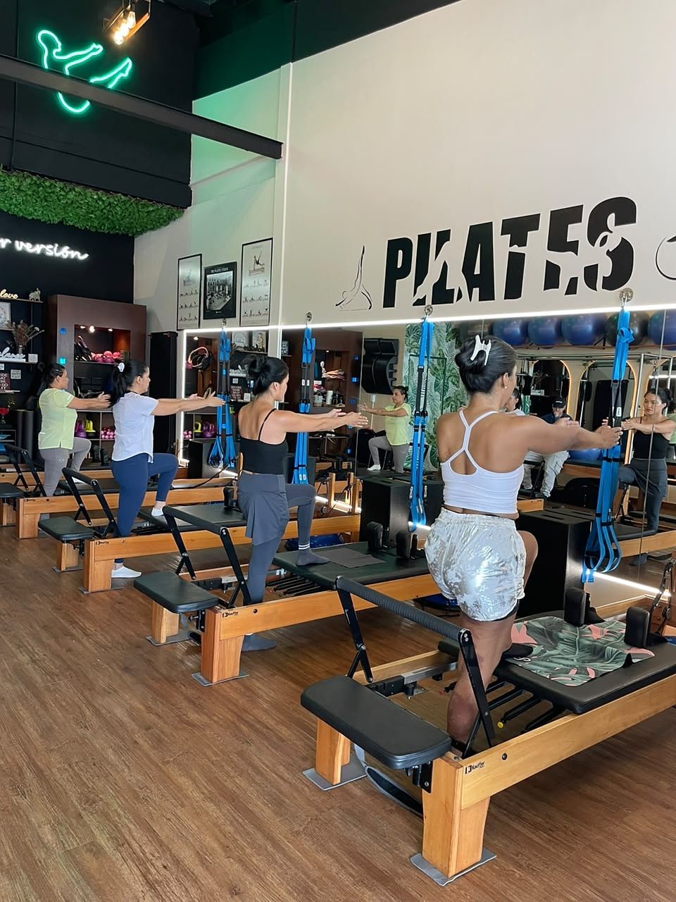 Alumnas de pie sobre el Reformer en zancada con los brazos extendidos al frente