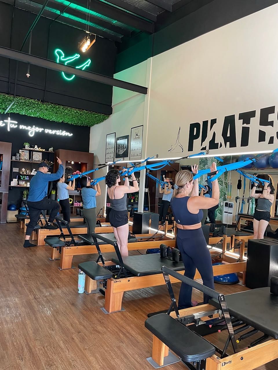 Clase grupal con TRX: alumnas de pie junto a las máquinas Reformer tirando de las correas de suspensión