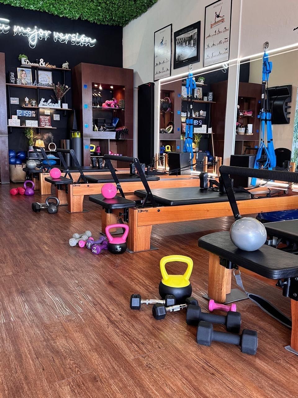 Kettlebells, mancuernas y balones de colores en el suelo junto a las máquinas Reformer