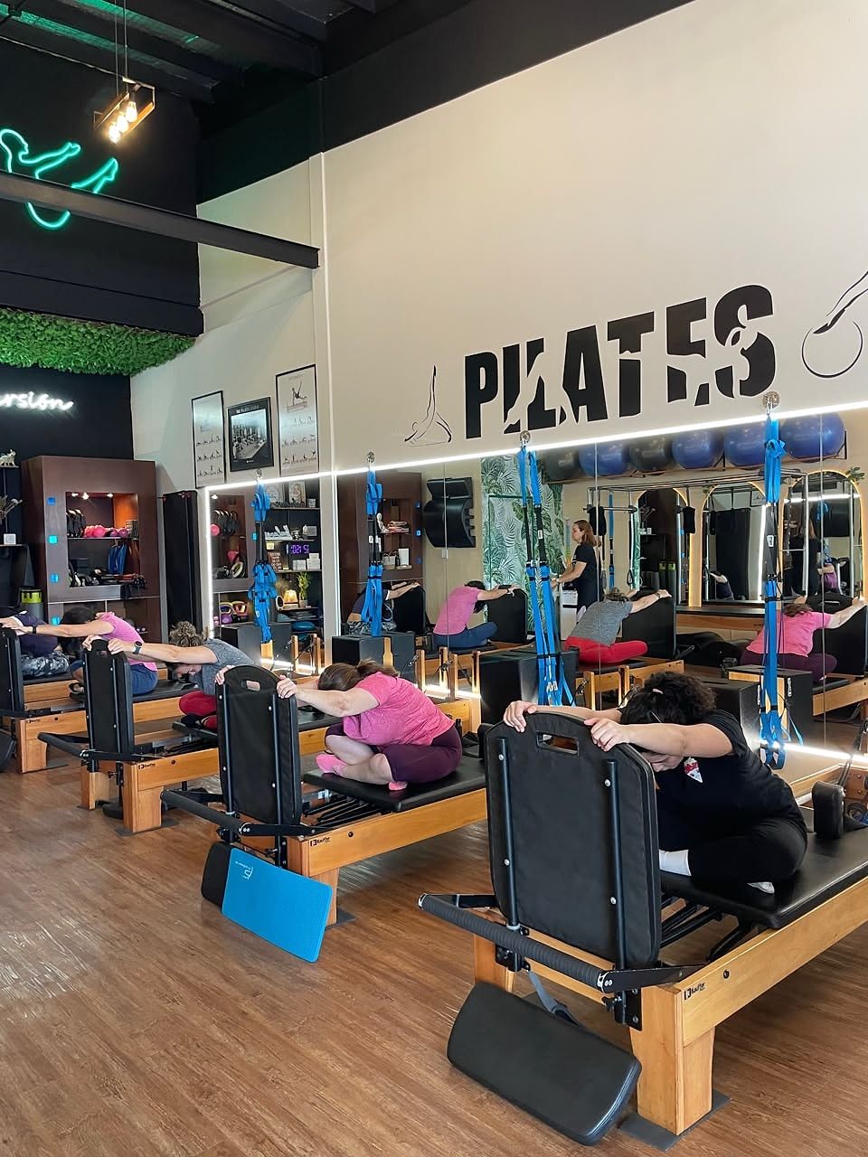 Alumnas estirando la espalda hacia delante sobre el Reformer, con la tabla de salto (Jumpboard) apoyada en el suelo