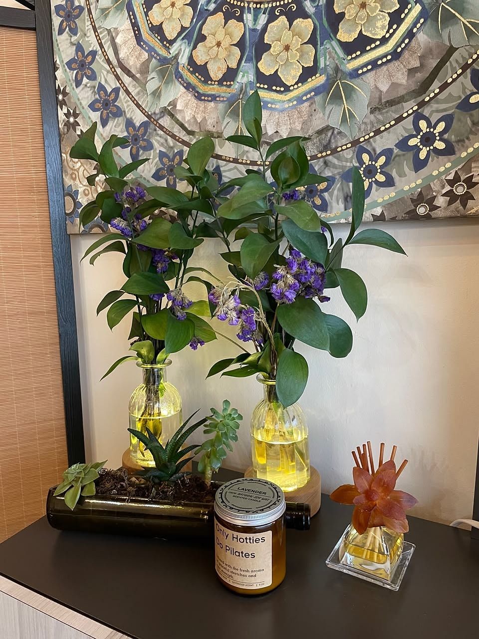 Rincón del estudio con flores moradas en jarrones, suculentas, una vela y un difusor de aroma
