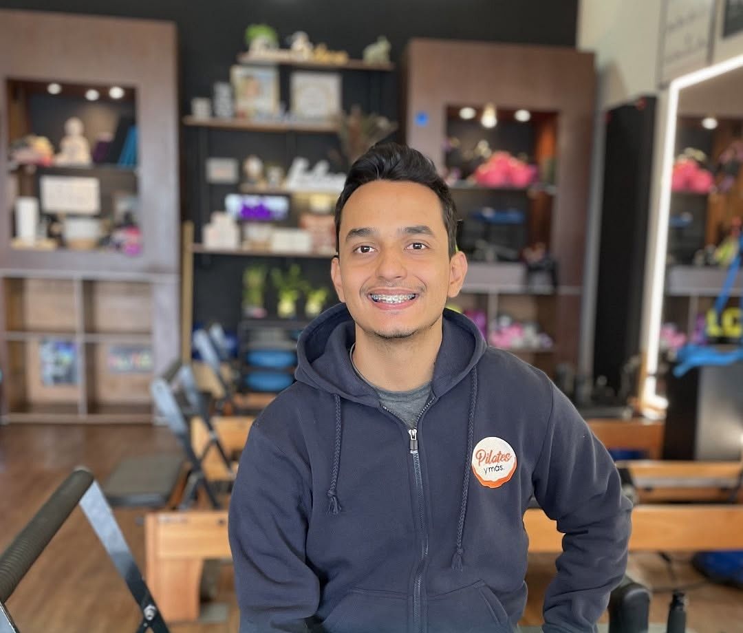 Cristian Silgado, instructor, sonriente sentado en un Reformer del estudio