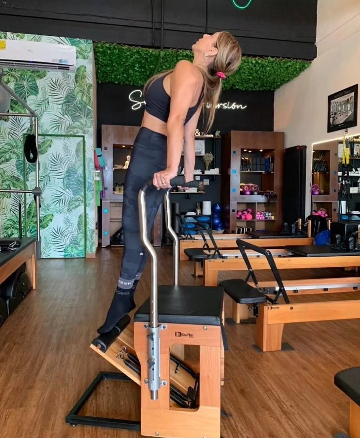Alumna de pie sobre la Chair, apoyada en las barras y elevando el cuerpo